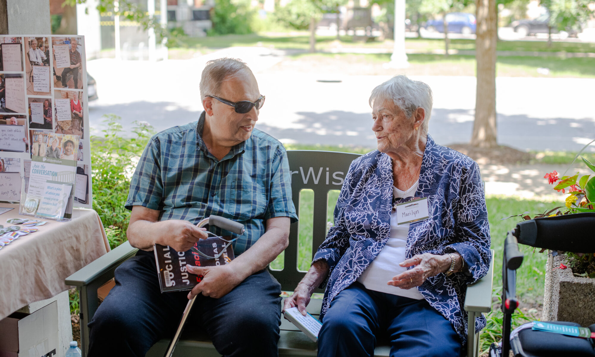 Senior man and woman sitting on the #ElderWisdom green bench having a conversation
